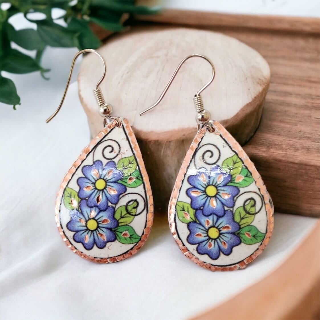 A pair of handmade blue flower drop copper circle earrings laid flat