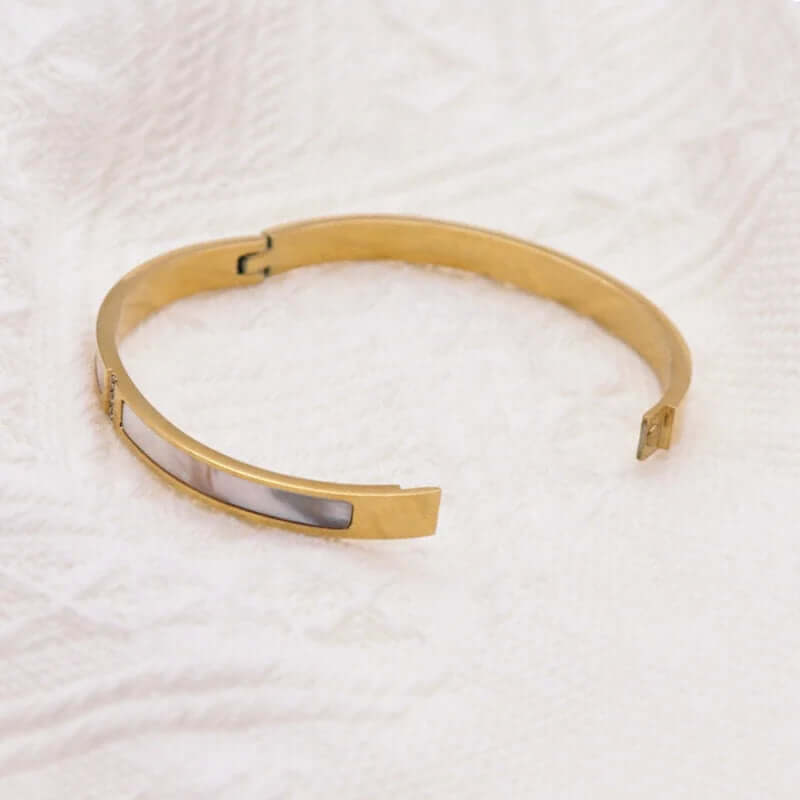 Gold bracelet with a silver tag on a white textured background