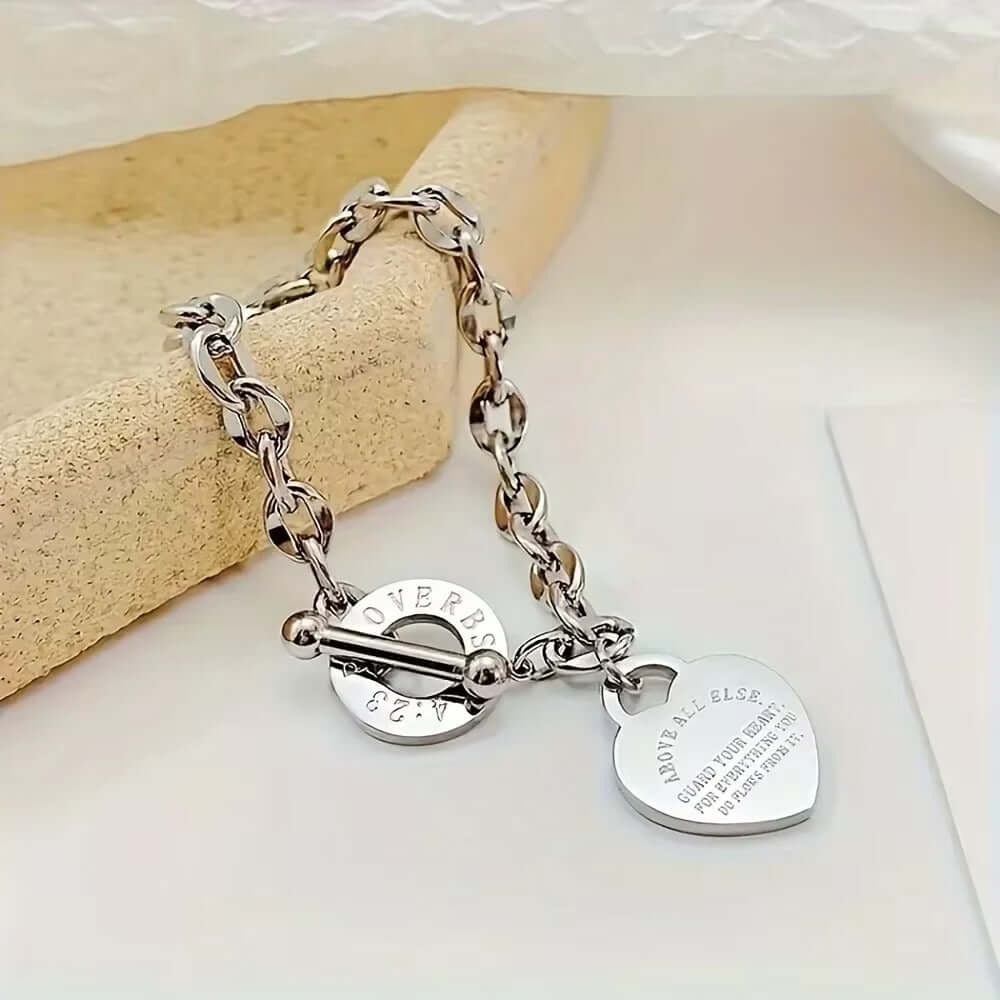 Angled view of heart charm chain bracelet with a steel toggle clasp