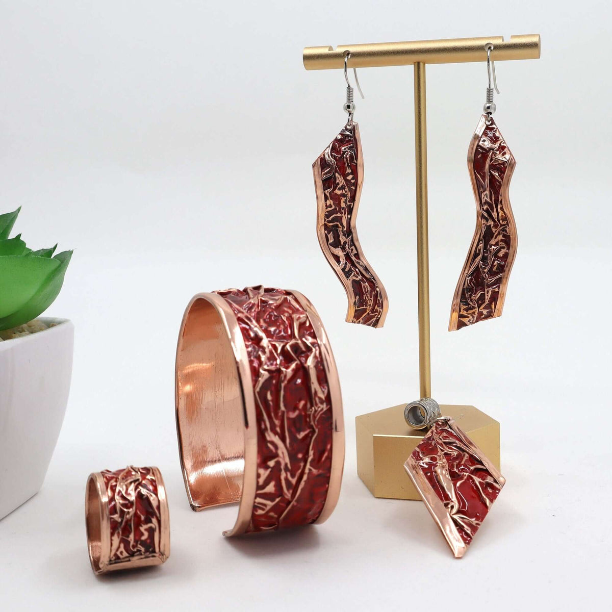 Individual pieces from four-piece red patterned wrinkled copper jewellery set arranged together