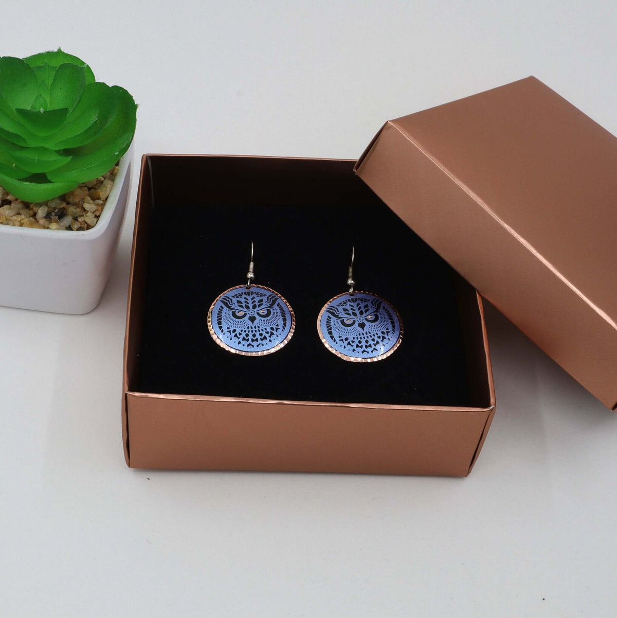 A pair of handcrafted blue owl copper circle earrings laid flat
