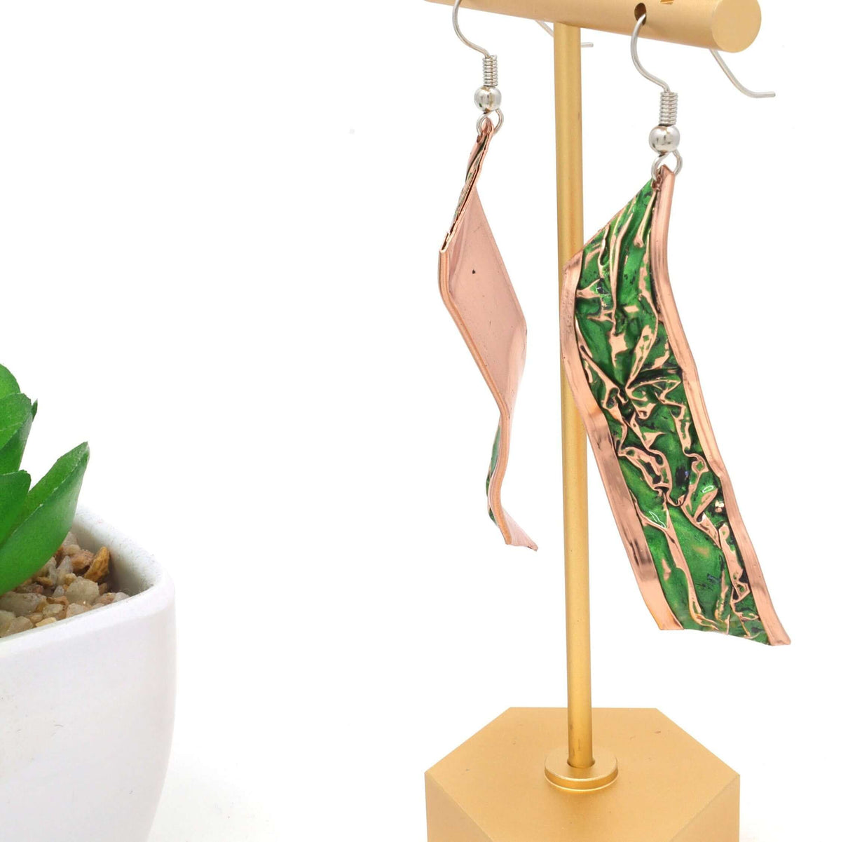 A pair of handcrafted artisan green wrinkled copper earrings laid flat