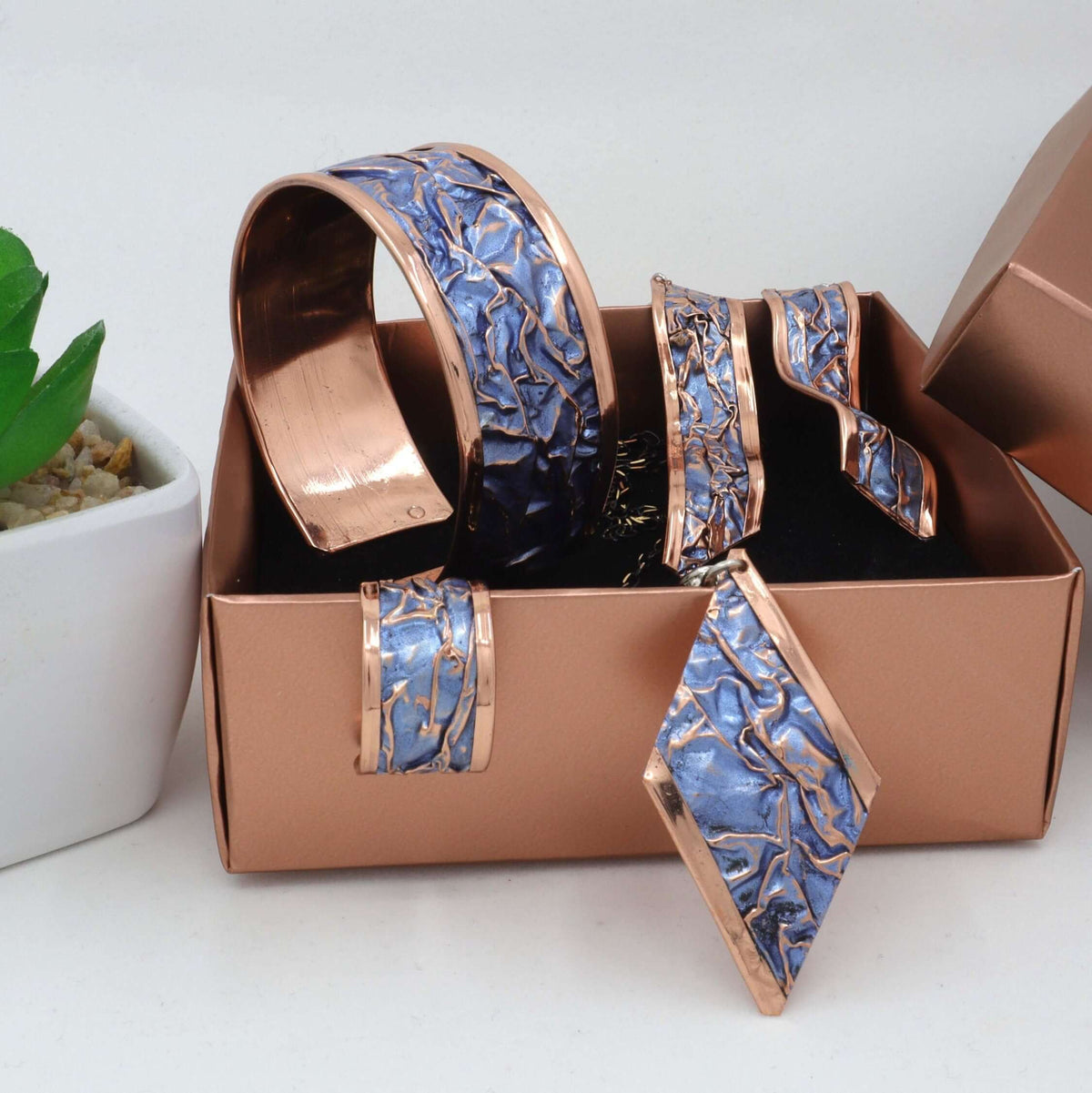 Handcrafted blue wrinkled copper jewellery set displayed on a plain background