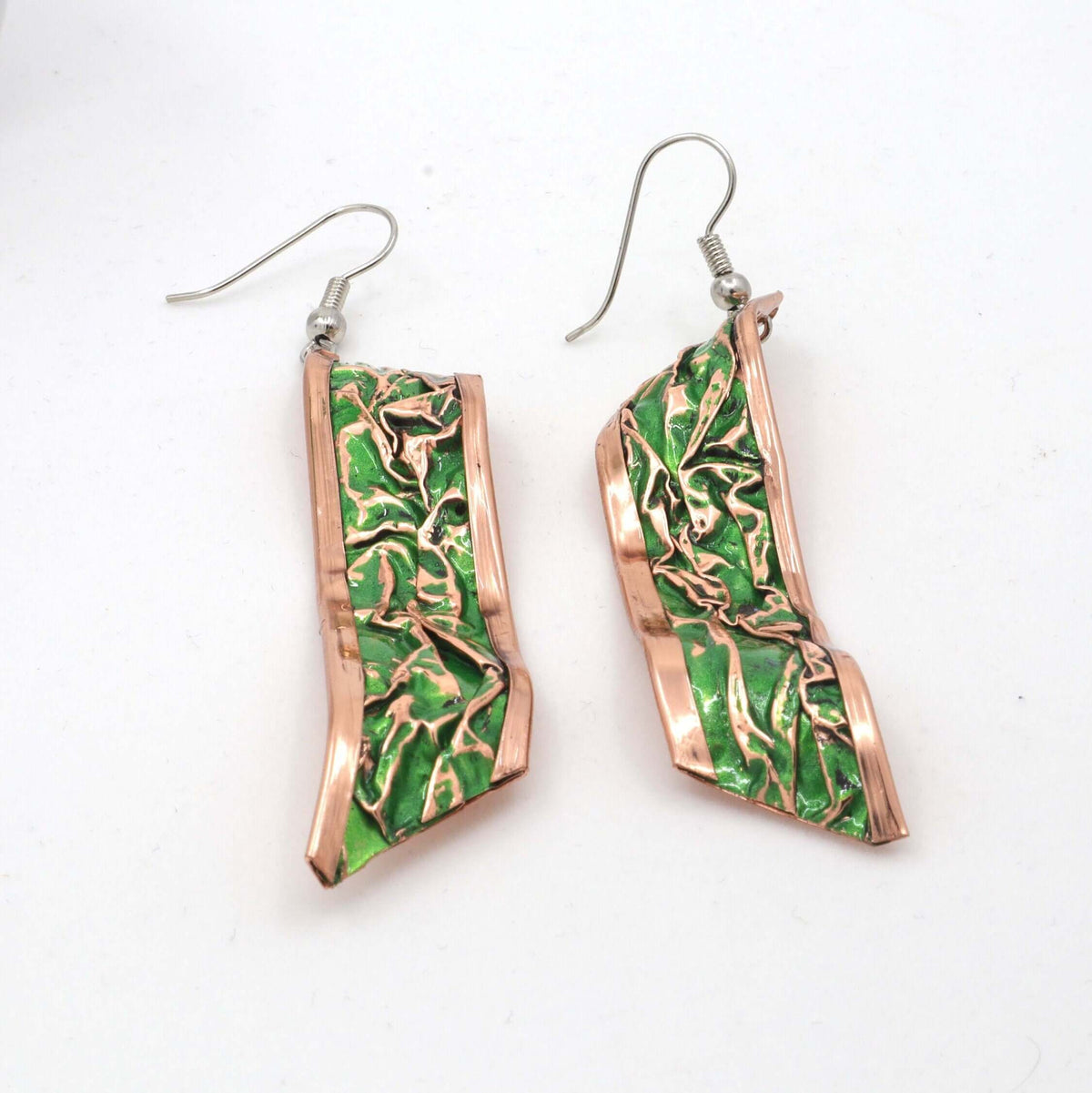 Handcrafted artisan green wrinkled copper earrings shown next to a hand for scale