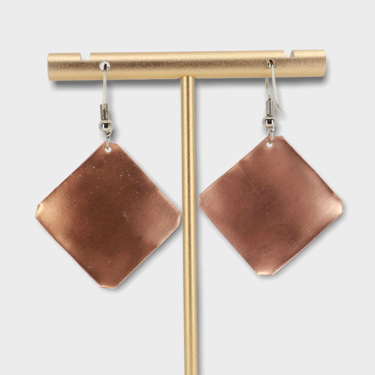 Handcrafted square yellow flower copper earrings shown next to a hand for scale