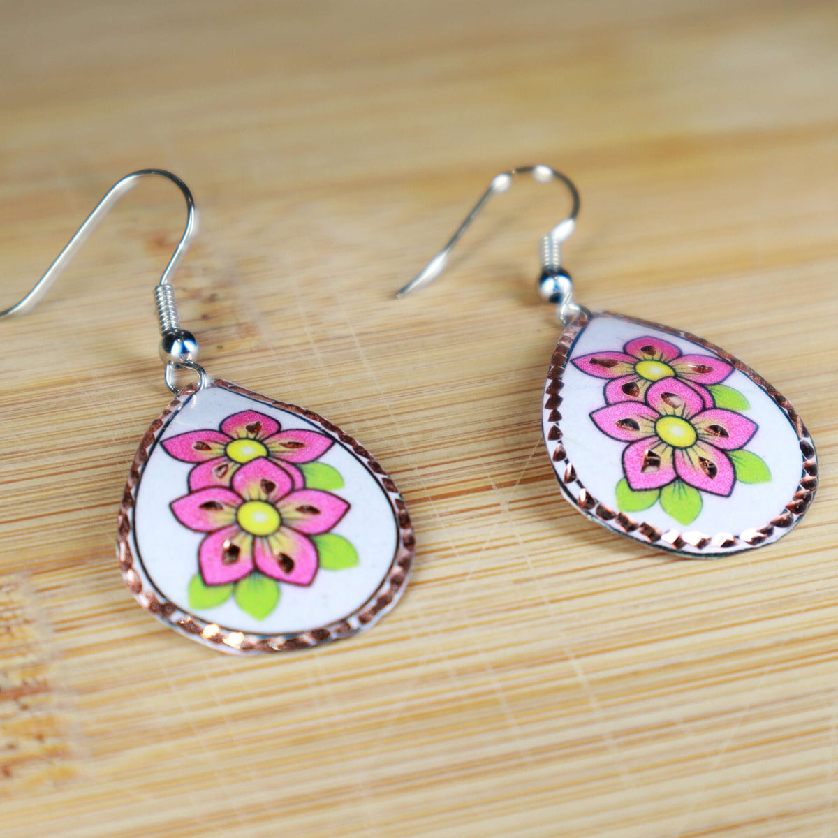 Handcrafted pink flower copper drop earrings shown next to a hand for scale