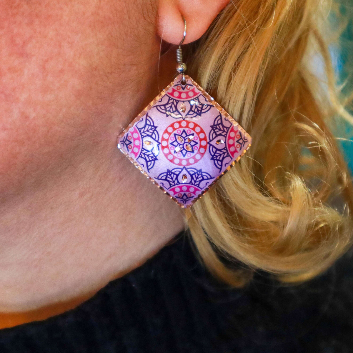 A pair of handcrafted artisan pink copper square earrings laid flat