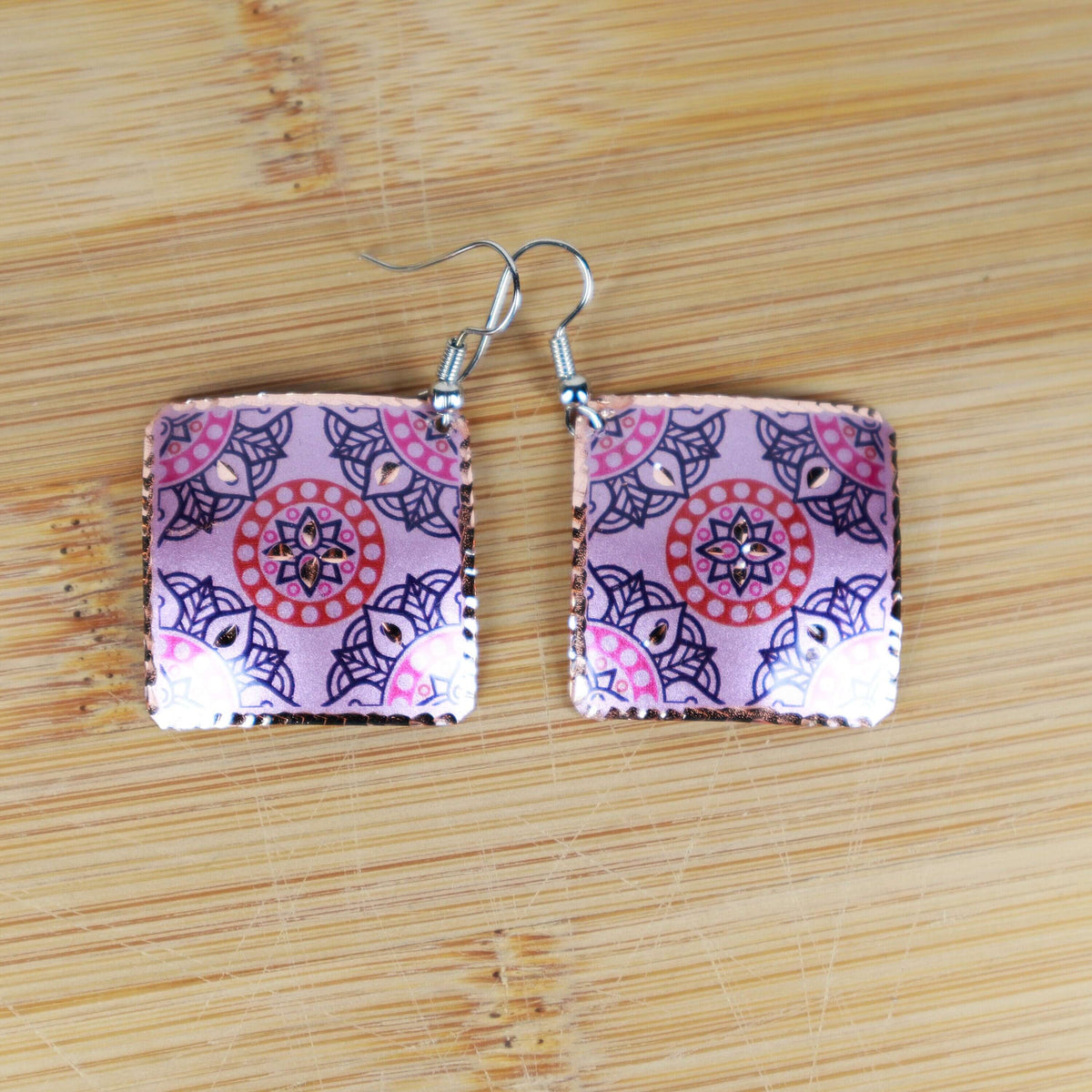 Handcrafted artisan pink copper square earrings shown next to a hand for scale